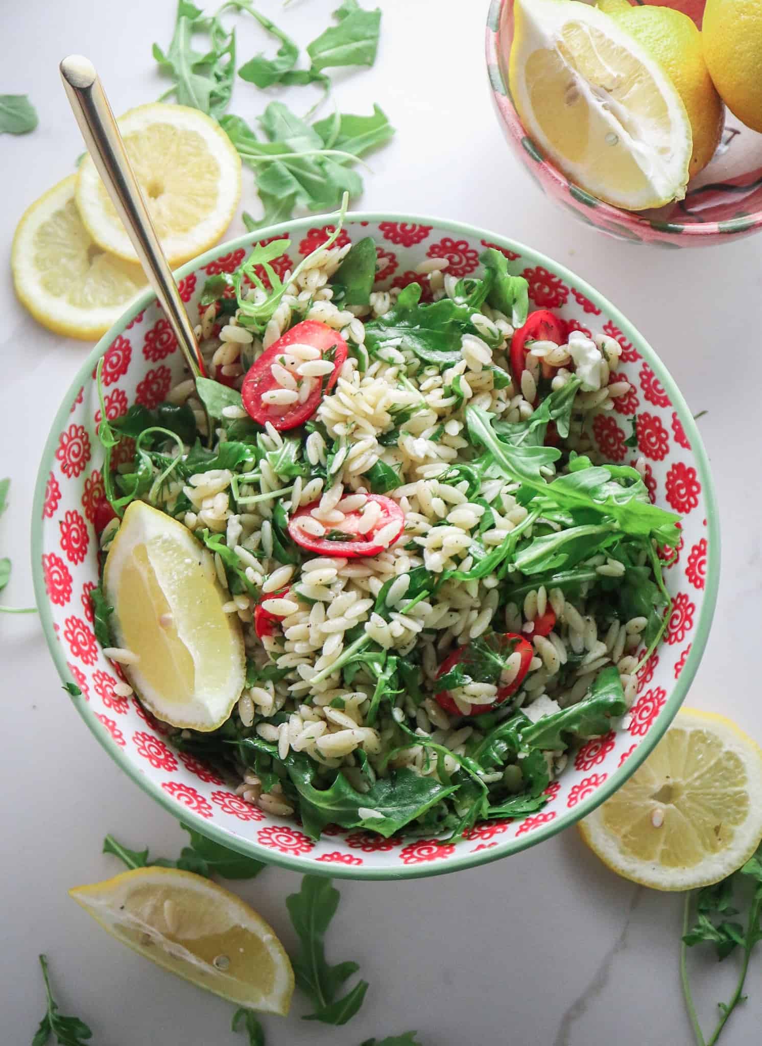 pasta salad with freshly squeezed lemon juice and herbs in a red bowl with fresh basil and lemon