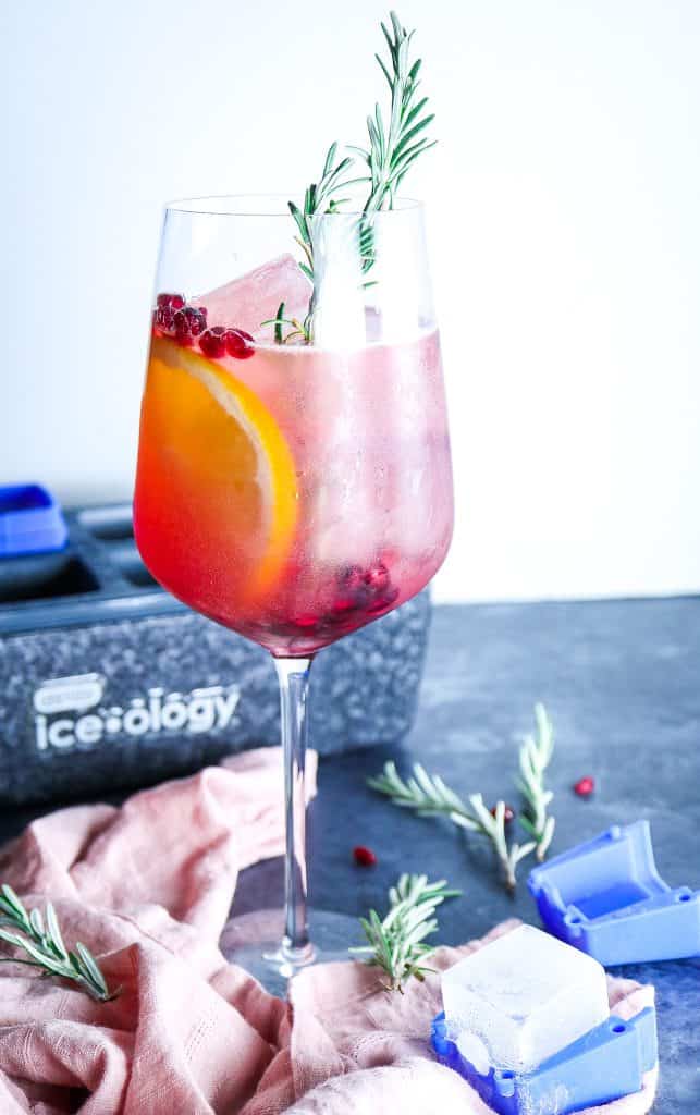 Orange Pomegranate Mocktail with pomegranate airily and fresh rosemary in a wine glass 