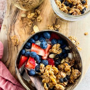 Almond Butter Blueberry Granola served with yogurt and fresh strawberries and blueberries in a bowl with a pink napkin