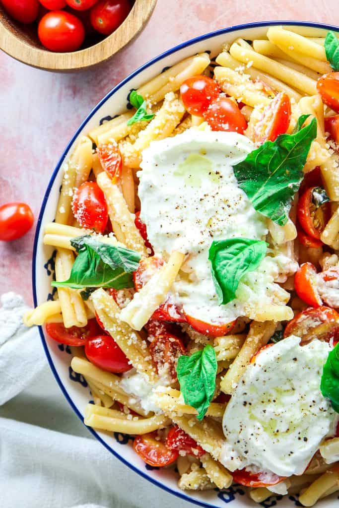 super easy summer pasta dish with fresh tomatoes and basil served in a big bowl with fresh burrata on top.