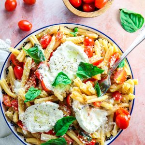 Simple summer pasta with tomatoes, basil, and burrata in a blue bowl with fresh basil on top