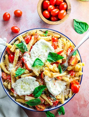 Simple summer pasta with tomatoes, basil, and burrata in a blue bowl with fresh basil on top