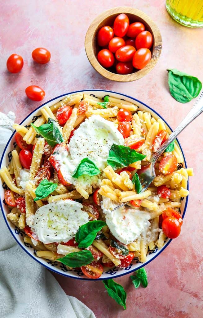 Simple summer pasta with tomatoes, basil, and burrata in a blue bowl with fresh basil on top