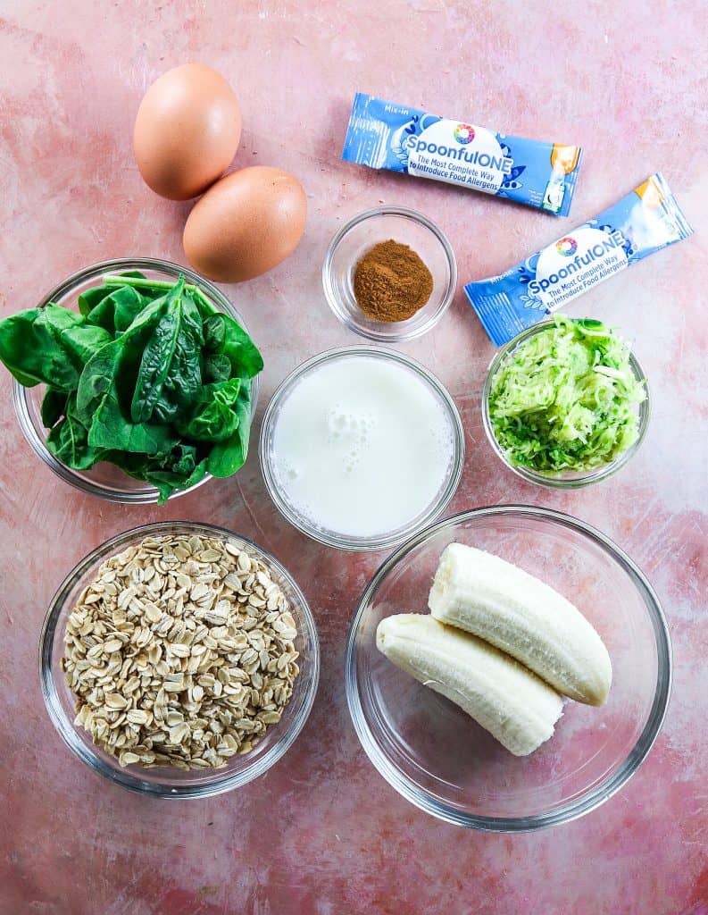 ingredients for veggie pancakes in bowls; banana, zucchini, oats, spinach, milk, cinnamon, eggs 