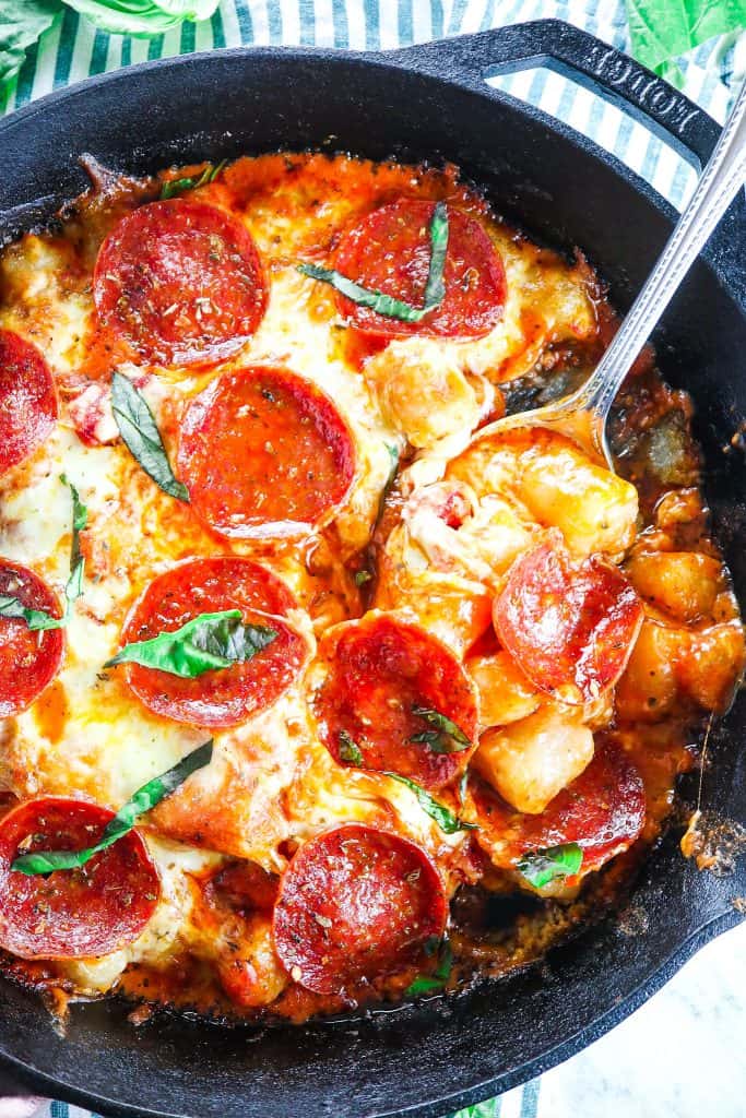 baked cauliflower gnocchi skillet with cheese and pepperoni topped with fresh basil