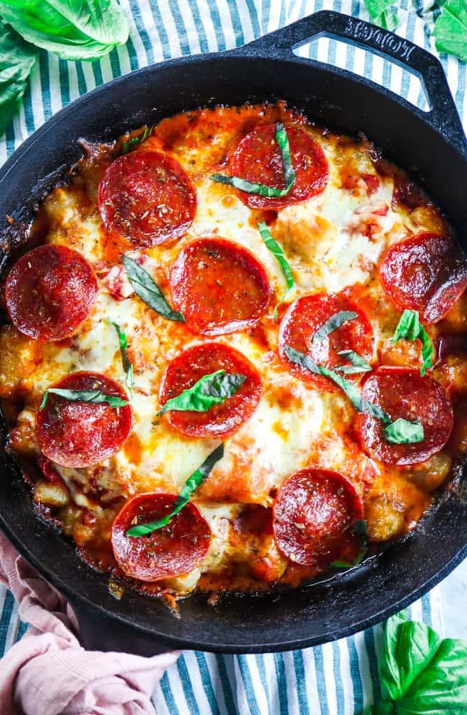 pepperoni pizza baked cauliflower gnocchi with cheese and fresh basil in a cast iron skillet on a striped napkin