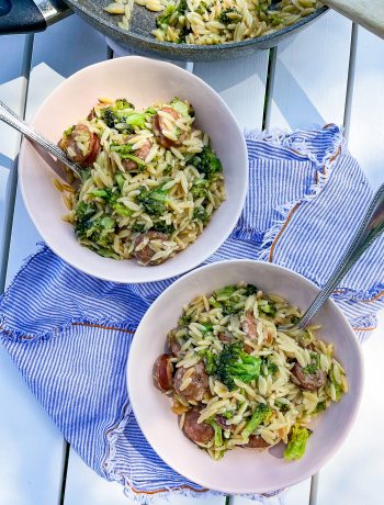 chicken sausage and broccoli orzo in bowls on a white table with fresh shaved parmesan cheese