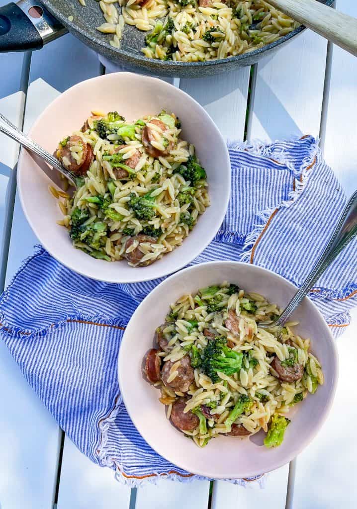 chicken sausage and broccoli orzo in bowls on a white table with fresh shaved parmesan cheese