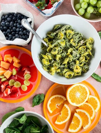 chicken and pesto tortellini salad in a white bowl with fresh fruit and salad