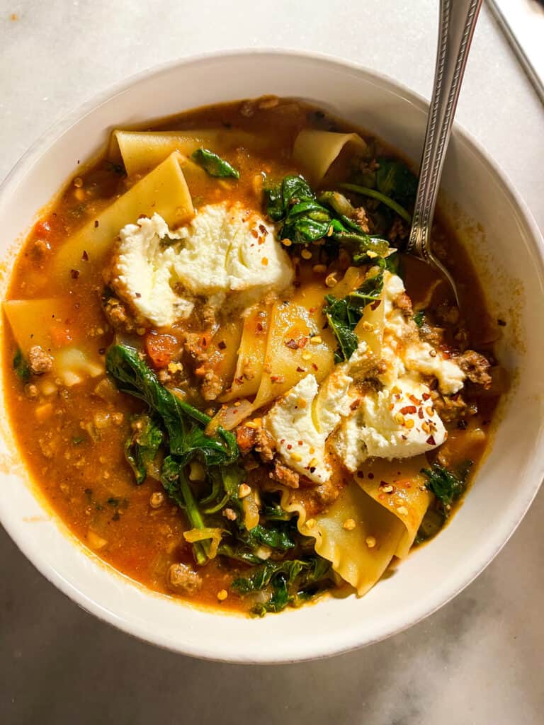 healthy lasagna soup in light pink bowls with ricotta, parmesan, and spinach