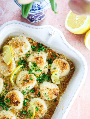 buttery garlic baked scallops in a white casserole dish with parsley and lemons