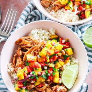 slow cooker bbq chicken over cauliflower rice topped with fresh mango salsa on a striped napkin with lime wedges