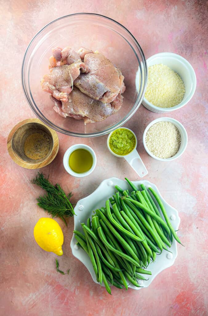 ingredients for pesto parmesan chicken, chicken thighs, green beans, lemon, dill, garlic powder, parmesan, panko breadcrumbs, pesto, and olive oil. 