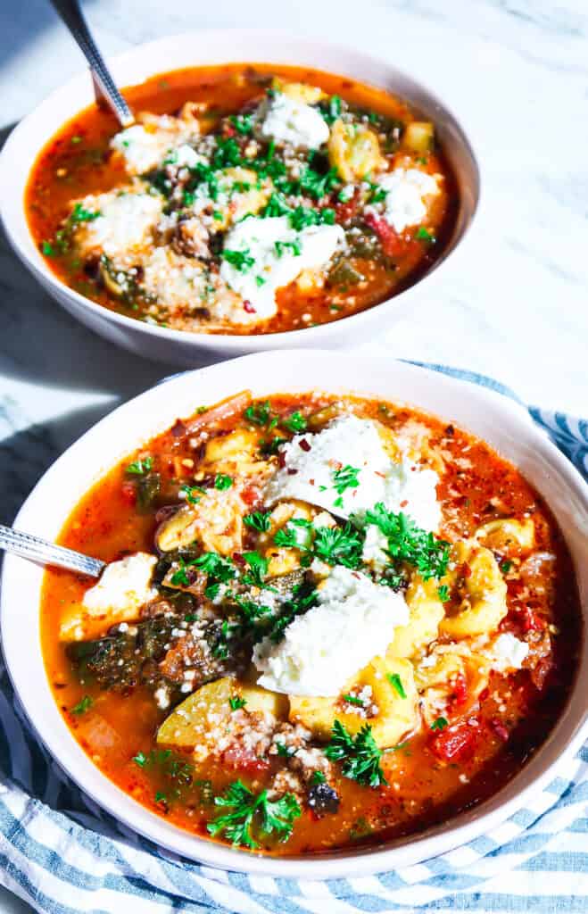 lasagna soup with tortellini in light pink bowls with a green striped napkin