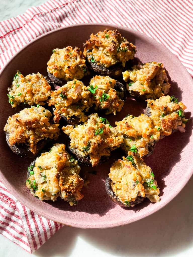 bacon and Boursin stuffed mushrooms with fresh chopped parsley on a pink plate with red striped napkin 