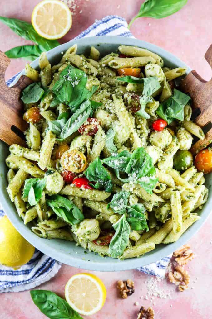pesto caprese penne pasta in a bowl with fresh basil, parmesan, and lemon on a blue striped dish towel