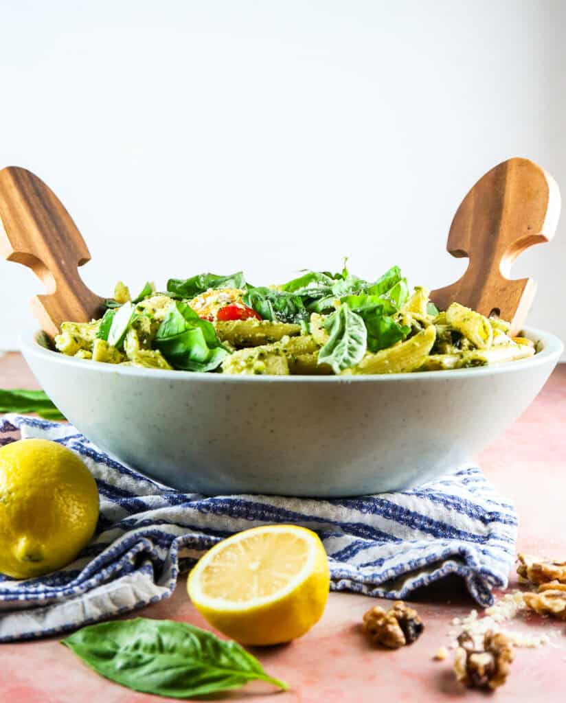 pesto caprese penne pasta in a sage green serving bowl with fresh lemon and basil