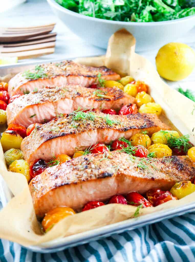 5 ingredient sheet pan salmon with cherry tomatoes and fresh dill on a striped napkin with a side of mixed greens 